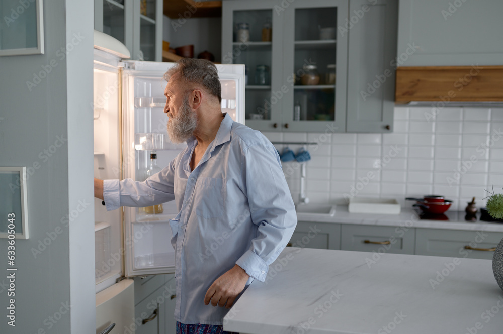Senior man hunger looking inside open fridge on kitchen