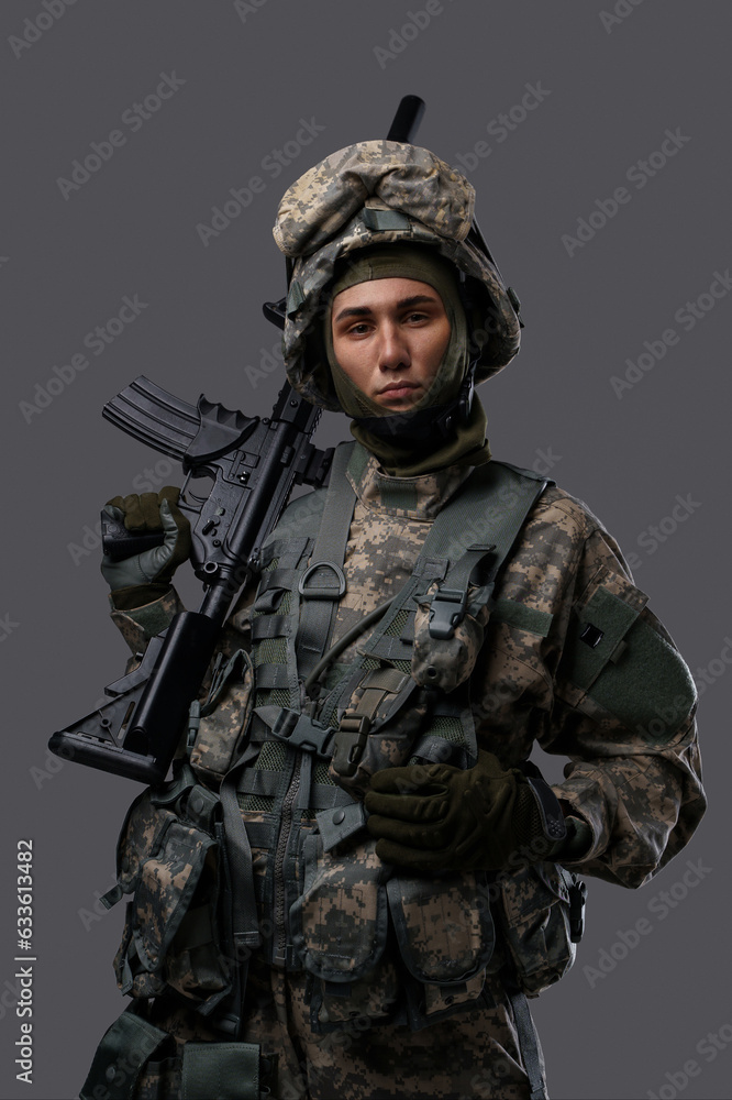Young soldier in uniform and helmet poses with a serious expression on a plain grey background, showcasing the strength and dedication of military personnel Young soldier in uniform and helmet poses with a serious expression on a plain grey background, showcasing the strength and dedication of military personnel