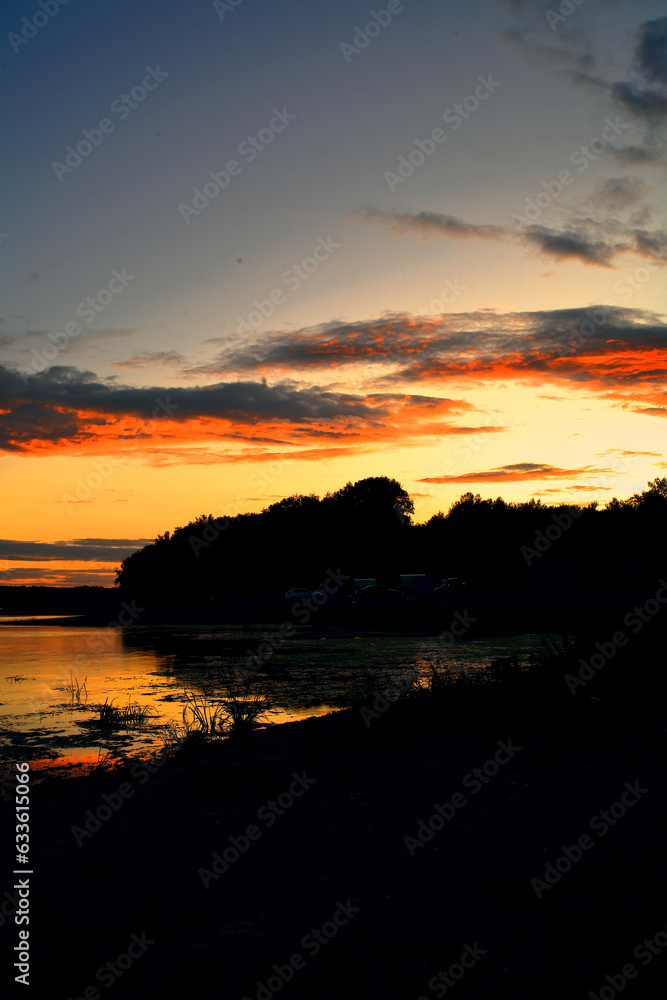 Sunset landscape over the water reflecting the sunset in the sea. behind the clouds and the blue sky over the lagoon.A beautiful panorama of the sky with glowing clouds.Red sun. river.	