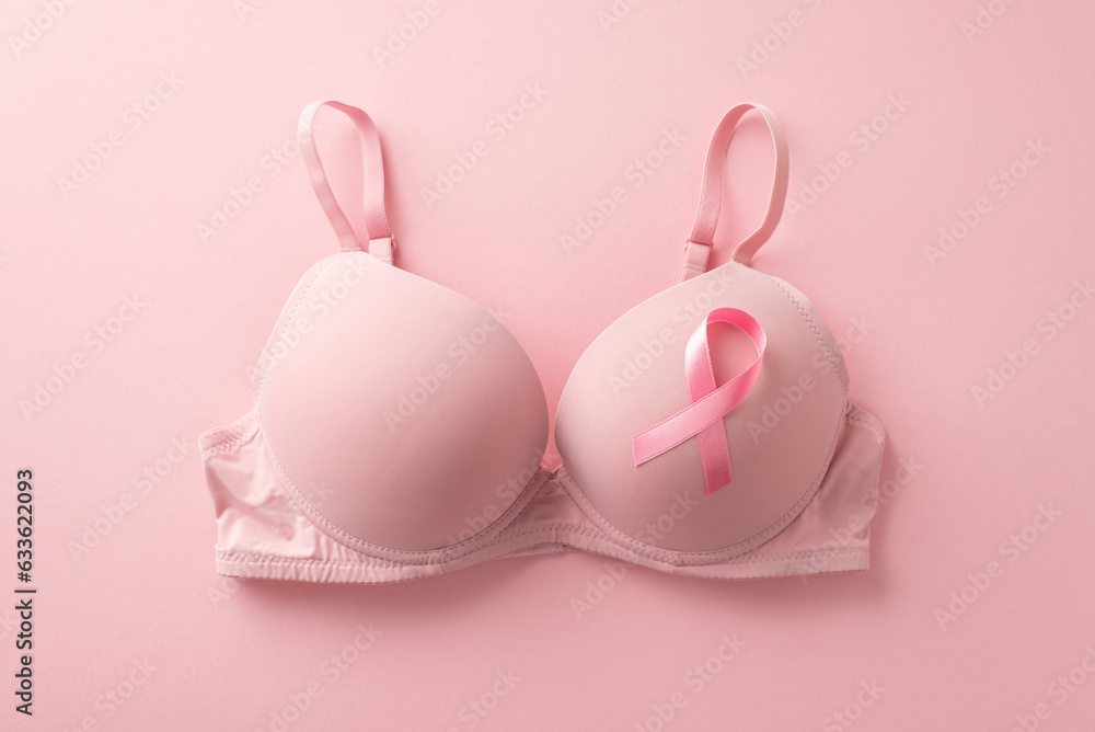 Uniting for breast cancer awareness. Top view photo showcasing a bra with attached pink ribbon symbol on soft pink backdrop. Perfect for promotional purposes or advertisements - obrazy, fototapety, plakaty 