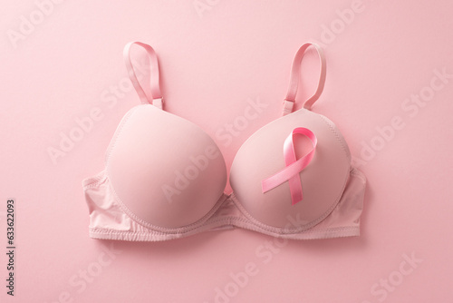 Uniting for breast cancer awareness. Top view photo showcasing a bra with attached pink ribbon symbol on soft pink backdrop. Perfect for promotional purposes or advertisements