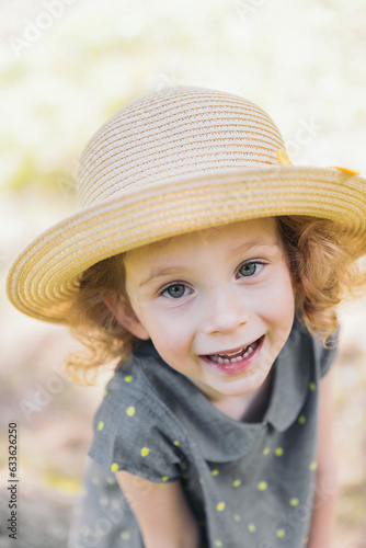 Close-up portrait of a girl. The girl is wearing a straw hat and a blouse with polka dots. The girl smiles. The background in the photo is light yellow.