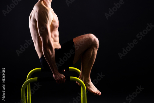 Fotografie Young muscular man doing parallel bar exercises in dark white red studio with co