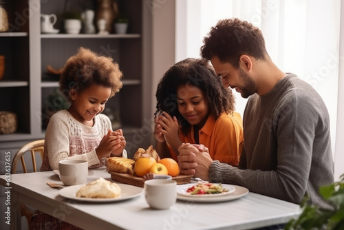 Happy multiracial family couple with children pray together before having morning breakfast at home together. Multiethnic parents with mixed race kids hold hands say prayer sit at kitchen table