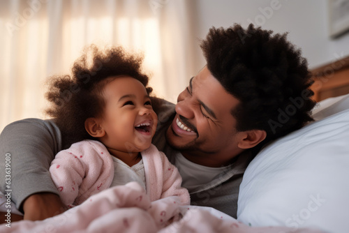 Happy loving young Black dad holding adorable mixed race baby daughter having fun in bed at home. Smiling African father playing with cute funny infant child girl waking up in bedroom in the morning