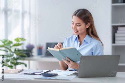 Smiling young happy Asian businesswoman working with laptop and documents in office. Accountant or beautiful asian female worker working happily in the office.