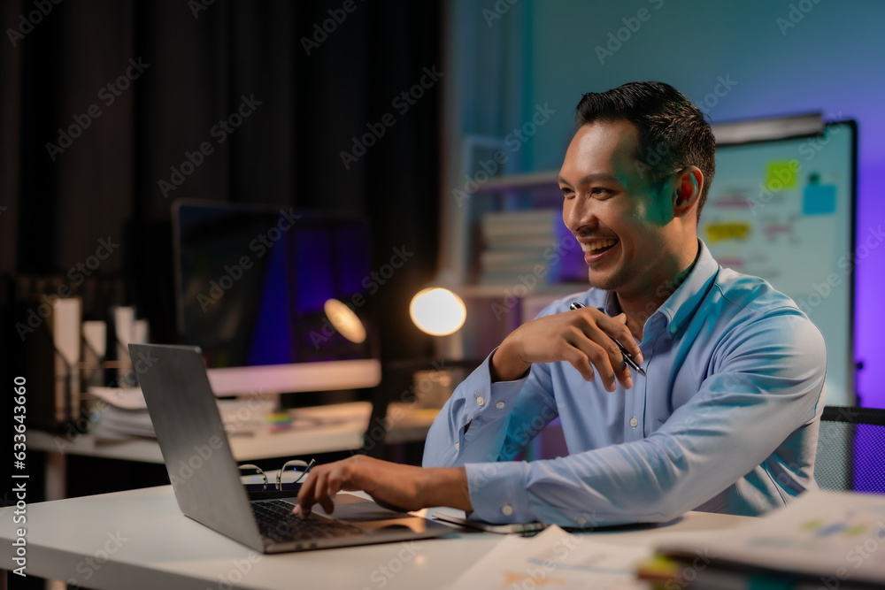 Commitment Asian businessman sitting at desk in office Working overtime late at night with document and laptop computer. Overtime work concept.