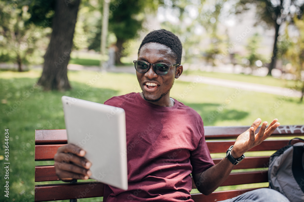 Fototapeta premium Young man sitting in the park relaxing in the nature and using digital tablet