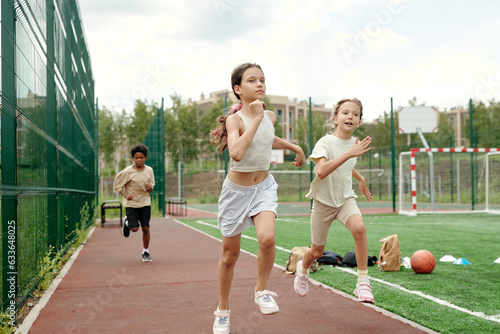 Active schoolgirl in white sportswear leading in running competition while moving along race track with intercultural classmates on background © pressmaster