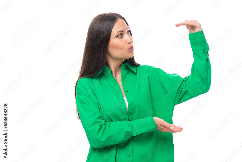 young european female model with well-groomed black hair and make-up dressed in a green shirt shows the size of the object on a white background with copy space young european female model with well-groomed black hair and make-up dressed in a green shirt shows the size of the object on a white background with copy space