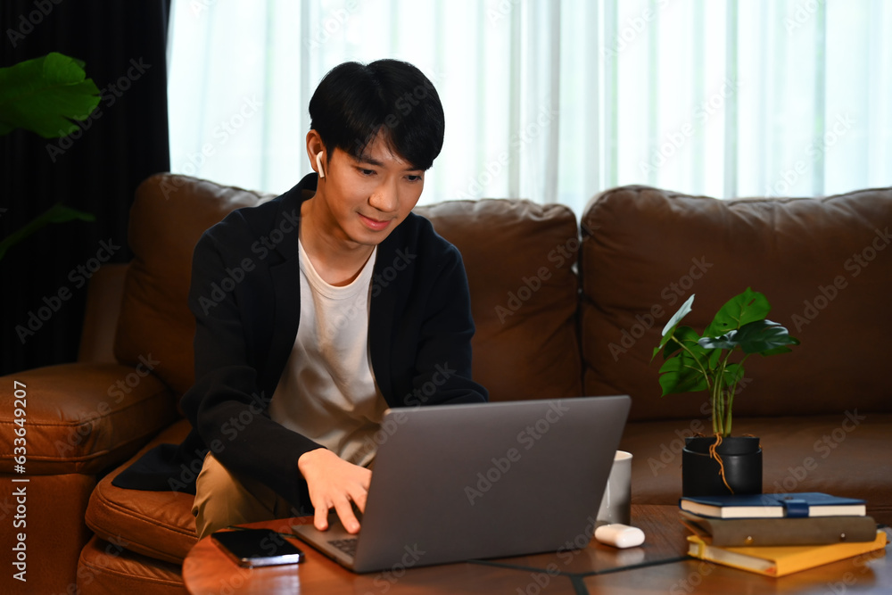 Naklejka premium Handsome male in smart casual wears browsing internet, remote work or stying online on laptop at home