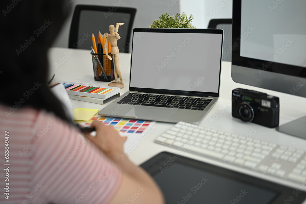 View over shoulder of female freelancer sitting at modern workplace and working with color swatch sample View over shoulder of female freelancer sitting at modern workplace and working with color swatch sample
