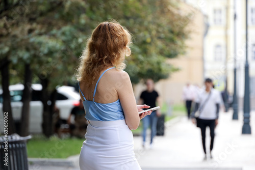 Woman with long hair standing with smartphone on a street on walking people background. Mobile communication in city © Oleg
