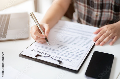 Close-up image of a woman signing her signature on a contract agreement at a table.