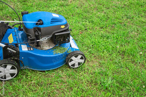 Lawn mower cutting grass. Small grass cuttings fly out of lawnmower. Grass clippings get spewed out of a mower pushed around by landscaper. CloseUp. Gardener working with mower machine. Mowing lawns  