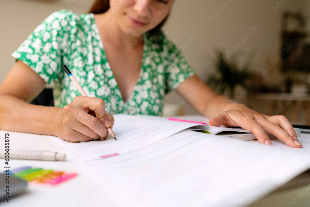 Adult university student woman sitting at the desk at home and doing homework, doing the exercise in the workbook, pencil in female hand. Adult university student woman sitting at the desk at home and doing homework, doing the exercise in the workbook, pencil in female hand.