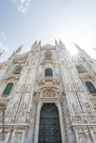 Milan Cathedral, Italian: Duomo di Milano, or Metropolitan Cathedral-Basilica of the Nativity of Saint Mary. View of main door and white marble facade on sunny summer day. Milan, Lombardy, Italy