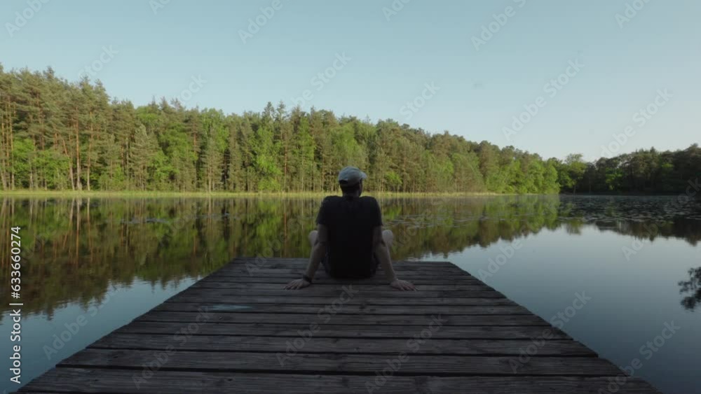Lac de Lispach, man sits back with arms behind looking out at calm reflection of lake Lac de Lispach, man sits back with arms behind looking out at calm reflection of lake