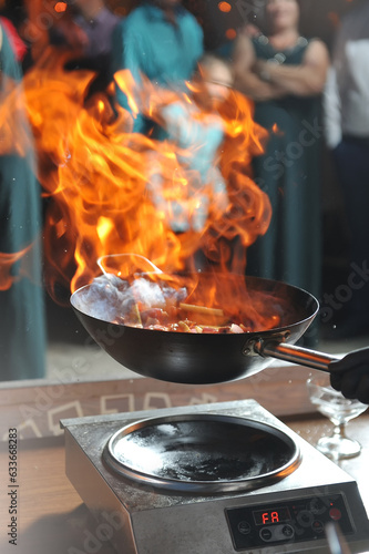 Cooking show by the chef with fire, fries meat in a frying pan and people looking it