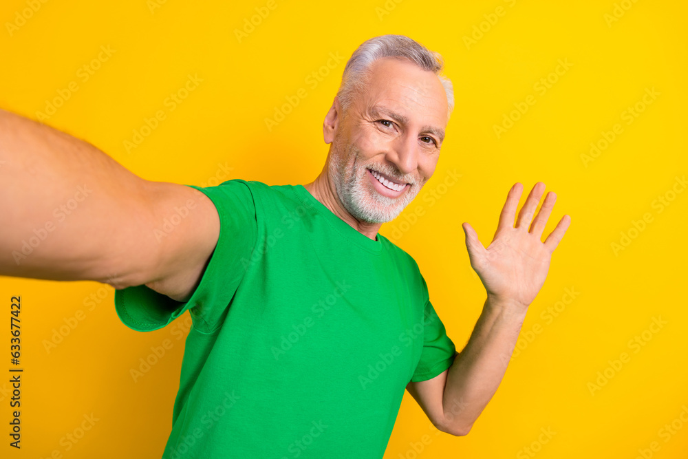 Portrait of cheerful aged man make selfie toothy smile arm palm waving recording video isolated on yellow color background Portrait of cheerful aged man make selfie toothy smile arm palm waving recording video isolated on yellow color background
