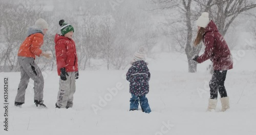 Children have fun outdoors during snowfall. Big family or friends playing at snowballs in winter park. Heavy snowfall