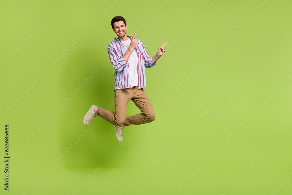 Full body photo of funky young man jump wear trendy clothes pointing fingers mockup black friday market isolated on green color background Full body photo of funky young man jump wear trendy clothes pointing fingers mockup black friday market isolated on green color background