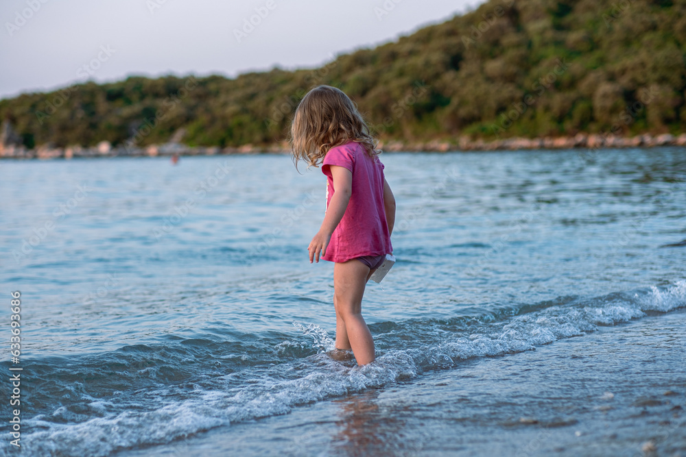 Little girl playing on the sea sandy beach. A girl in a pink t-shirt and swimming trunks on a beautiful sea beach. Cleanest tranquise water of Adriatic sea. Little girl playing on the sea sandy beach. A girl in a pink t-shirt and swimming trunks on a beautiful sea beach. Cleanest tranquise water of Adriatic sea.