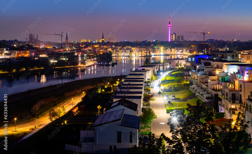 Night panorama of Dortmund Germany. Former blast furnace site and new recreational area in Hoerde called “Phoenixsee“. TV-Tower and skyline in the background after colorful sunset in springtime. Night panorama of Dortmund Germany. Former blast furnace site and new recreational area in Hoerde called “Phoenixsee“. TV-Tower and skyline in the background after colorful sunset in springtime.