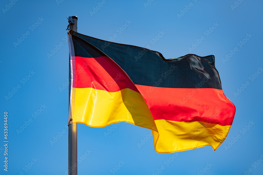German flag in black-red-gold color on a sunny day in Germany. National yymbol of the “Bundesrepublik Deutschland“. Flag pole and wavy fabric blown in the wind on a blue sky day. Intense sunlit colors German flag in black-red-gold color on a sunny day in Germany. National yymbol of the “Bundesrepublik Deutschland“. Flag pole and wavy fabric blown in the wind on a blue sky day. Intense sunlit colors