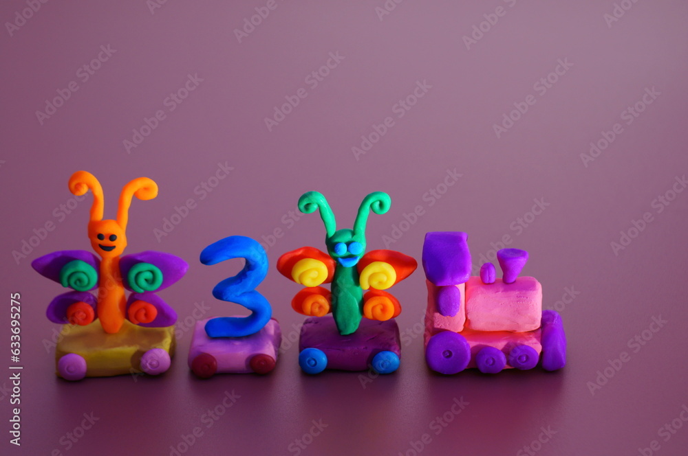 Naklejka premium Toy train made of plasticine with butterflies and the number 3. Birthday. A festive event. Color background.