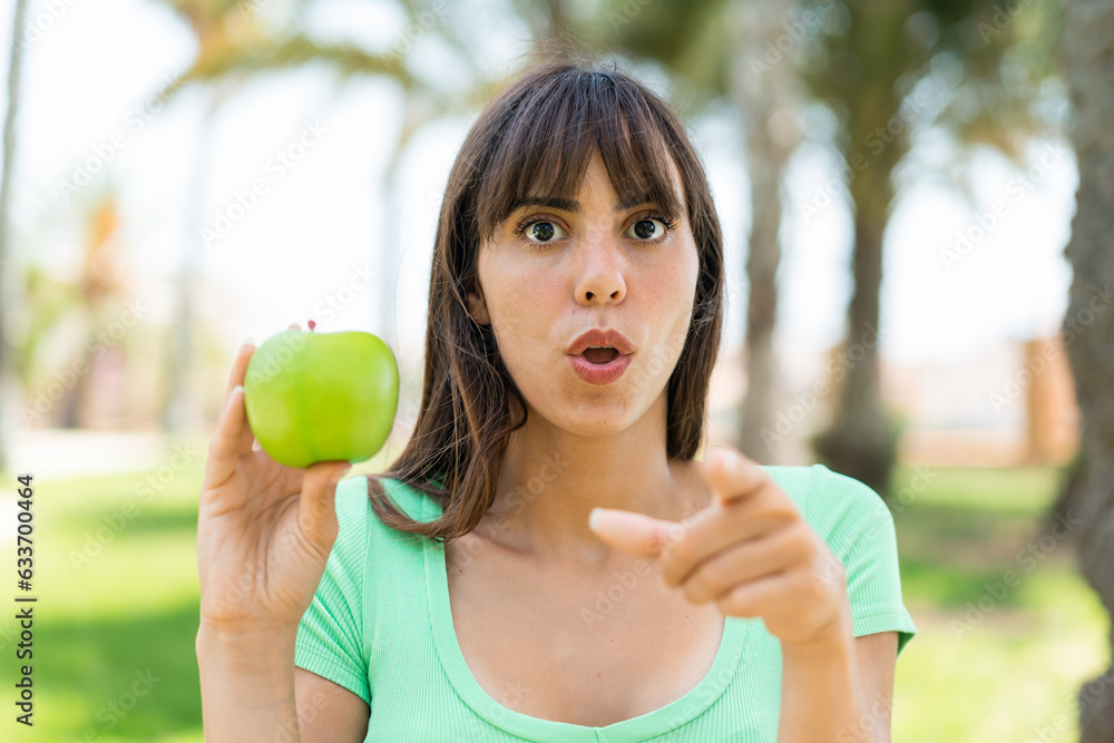 Young woman with an apple at outdoors surprised and pointing front Young woman with an apple at outdoors surprised and pointing front