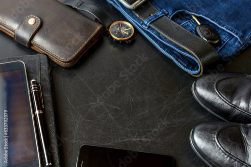 Men's accessories (notebook, pen, phone, shoes, wrist watches, wallet, purse, belt, jeans, pants, shoes) on a black board.