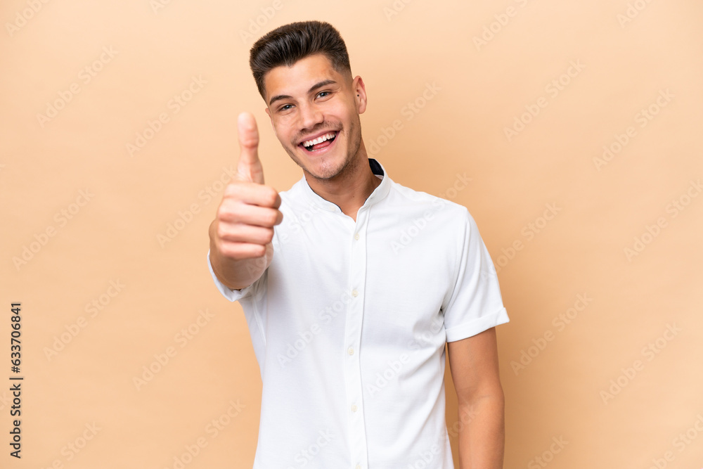 Young caucasian man isolated on beige background with thumbs up because something good has happened Young caucasian man isolated on beige background with thumbs up because something good has happened