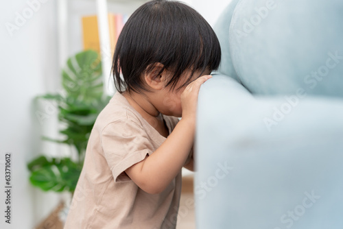 little asian children kid playing hide and seek standing behind the sofa, Adorable child having fun in the home. happy family have fun with kids, activity, learning, activity, game, meditation.