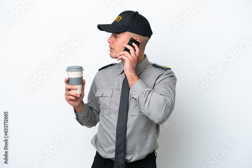 Young caucasian security man isolated on white background holding coffee to take away and a mobile