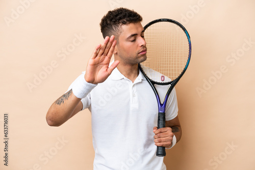 Young brazilian handsome man playing tennis isolated on beige background making stop gesture and disappointed © luismolinero