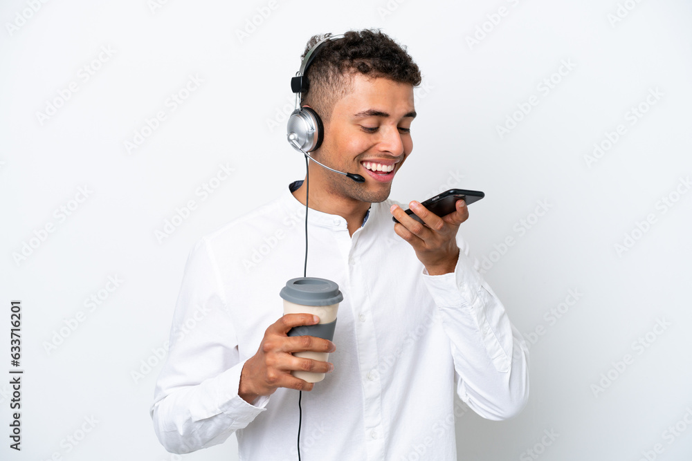 Telemarketer Brazilian man working with a headset isolated on white background holding coffee to take away and a mobile Telemarketer Brazilian man working with a headset isolated on white background holding coffee to take away and a mobile