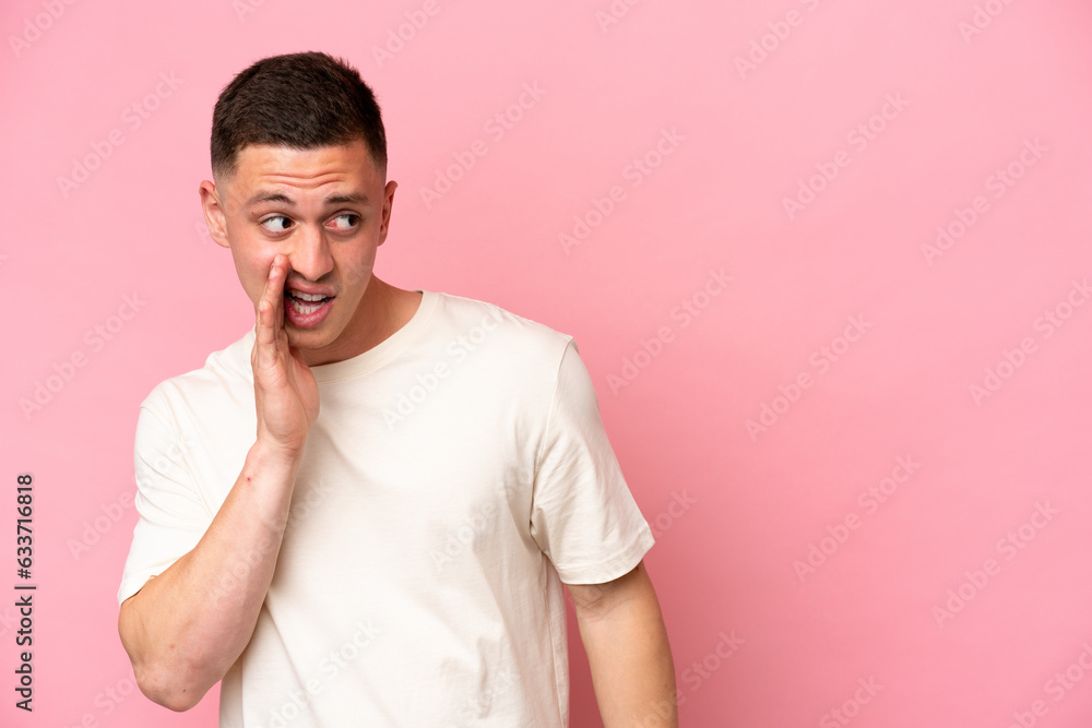Young Brazilian man isolated on pink background whispering something with surprise gesture while looking to the side Young Brazilian man isolated on pink background whispering something with surprise gesture while looking to the side