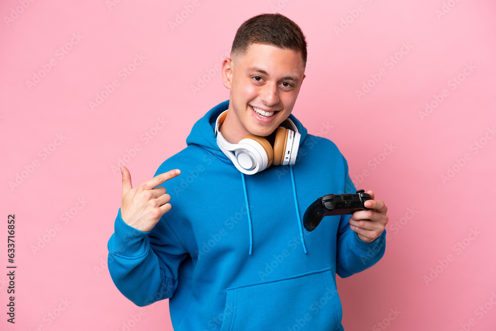 Young brazilian man playing with a video game controller isolated on pink background giving a thumbs up gesture Young brazilian man playing with a video game controller isolated on pink background giving a thumbs up gesture