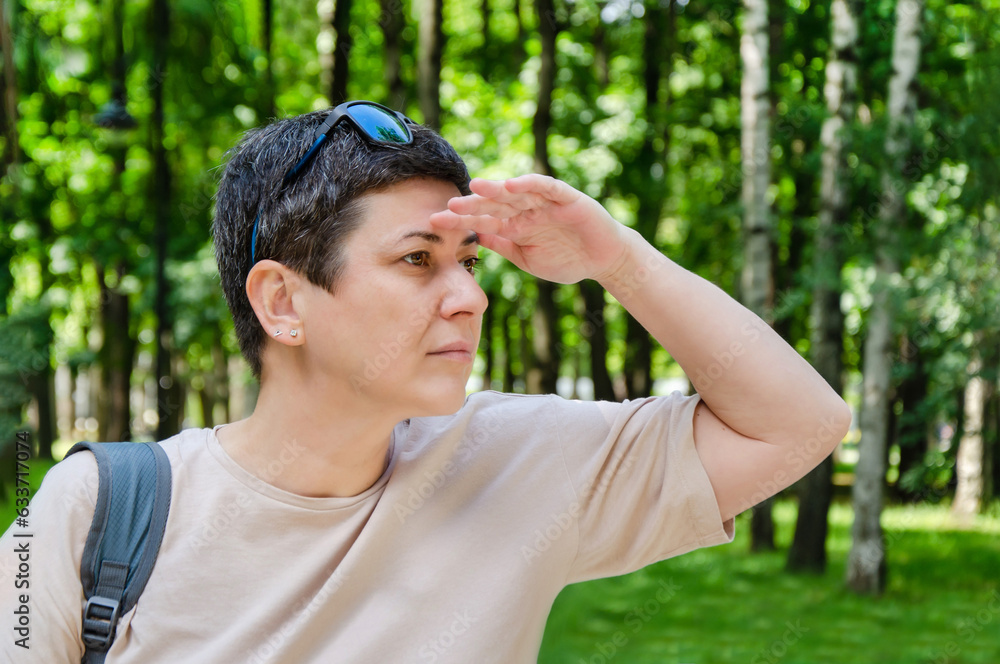 woman looks into distance, covering her eyes from sunlight with her palm while walking in the park woman looks into distance, covering her eyes from sunlight with her palm while walking in the park