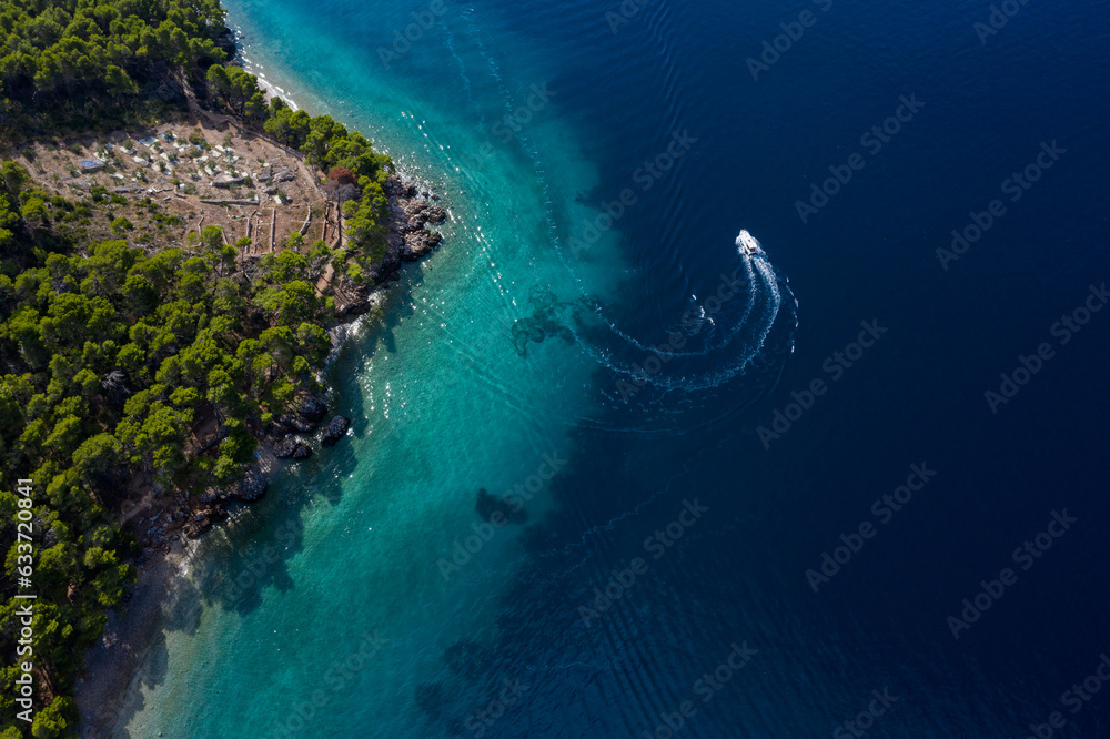 Tourist boat on the emerald sea from a bird's eye view, beautiful coastline covered with thick trees. Makarska riviera in Dalmatia, Croatia