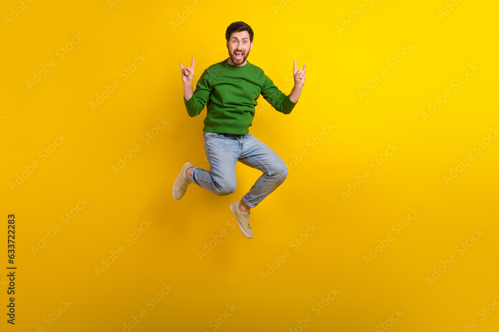 Full size body photo of jump trampoline crazy guy fingers showing rock roll punk gesturing singing isolated on yellow color background