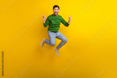 Full size body photo of jump trampoline crazy guy fingers showing rock roll punk gesturing singing isolated on yellow color background