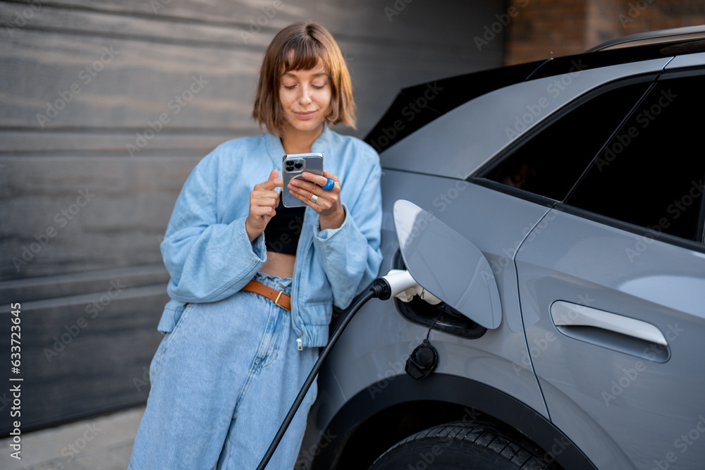 Young woman using smartphone leaning to her car and waiting while it charges. Concept of new technologies and modern lifestyle