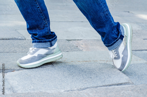 Konstfotografi woman's feet in jeans and sneakers tripping over unevenly laid paving slabs