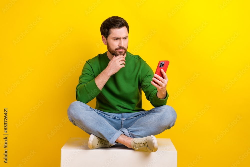 Full size photo of thoughtful young businessman touch chin decide browsing smartphone fresh news media isolated on yellow color background Full size photo of thoughtful young businessman touch chin decide browsing smartphone fresh news media isolated on yellow color background