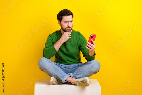 Full size photo of thoughtful young businessman touch chin decide browsing smartphone fresh news media isolated on yellow color background