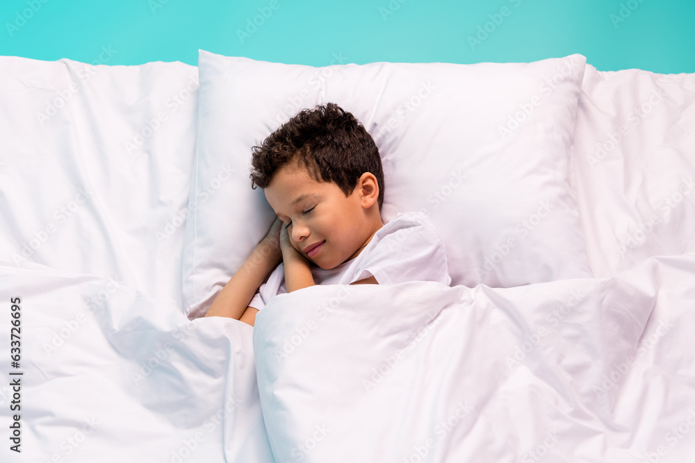 Above view portrait of peaceful schoolkid laying sleeping comfy bed sheets pillow covered blanket isolated on turquoise background Above view portrait of peaceful schoolkid laying sleeping comfy bed sheets pillow covered blanket isolated on turquoise background