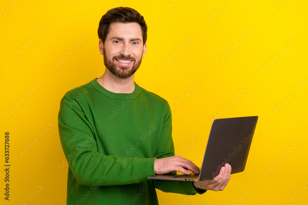 Photo of handsome young businessman wearing green stylish pullover holding netbook digital technology isolated on yellow color background Photo of handsome young businessman wearing green stylish pullover holding netbook digital technology isolated on yellow color background