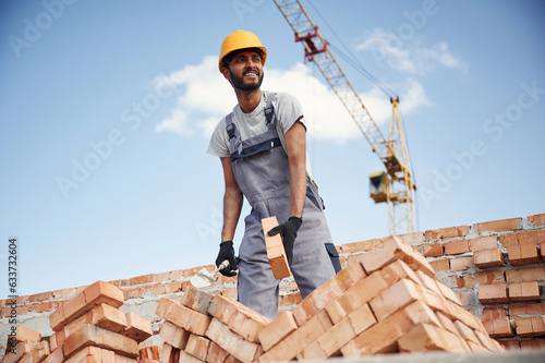 Working against blue sky. Handsome Indian man is on the construction site